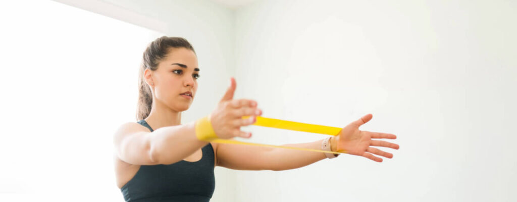 why physical therapy is crucial after a shoulder dislocation, a woman uses a yellow exercise band to strengthen shoulder