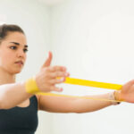 why physical therapy is crucial after a shoulder dislocation, a woman uses a yellow exercise band to strengthen shoulder